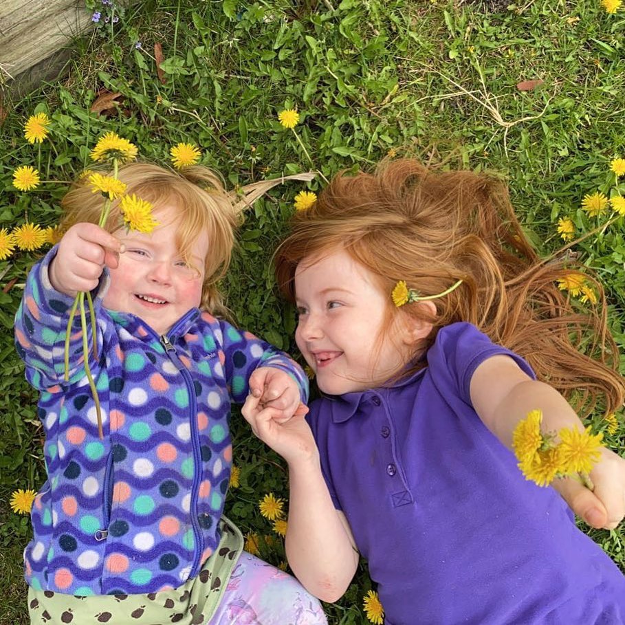 Two kids laying in the grass surrounded by dandelions